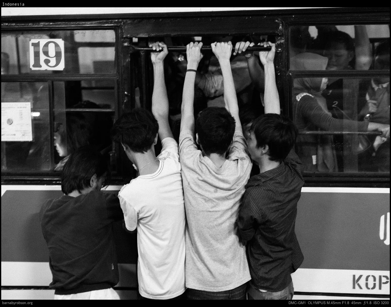 Four young men from behind, holding onto a bus window.