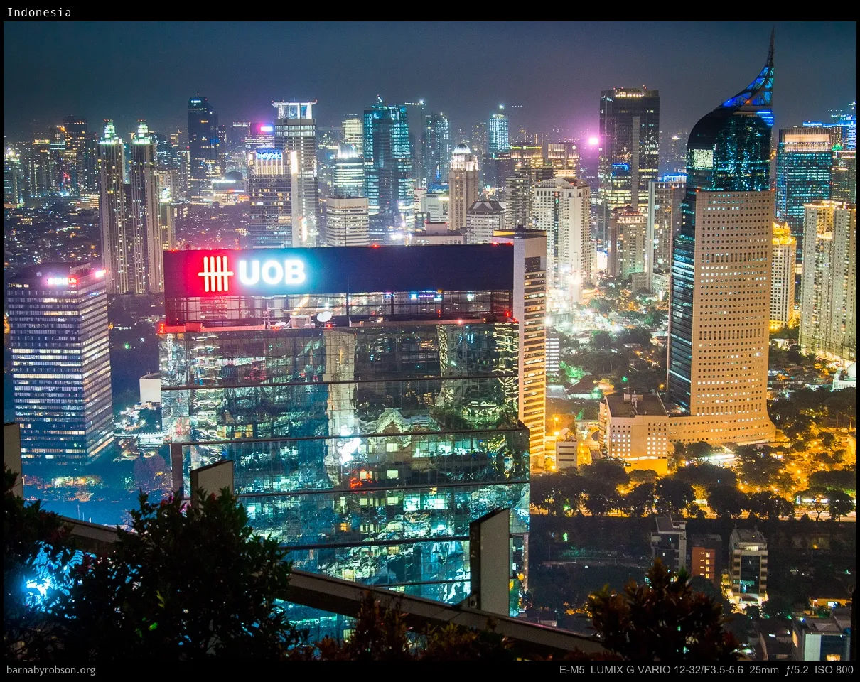 City skyline at night, illuminated buildings, prominent UOB sign, and reflections.