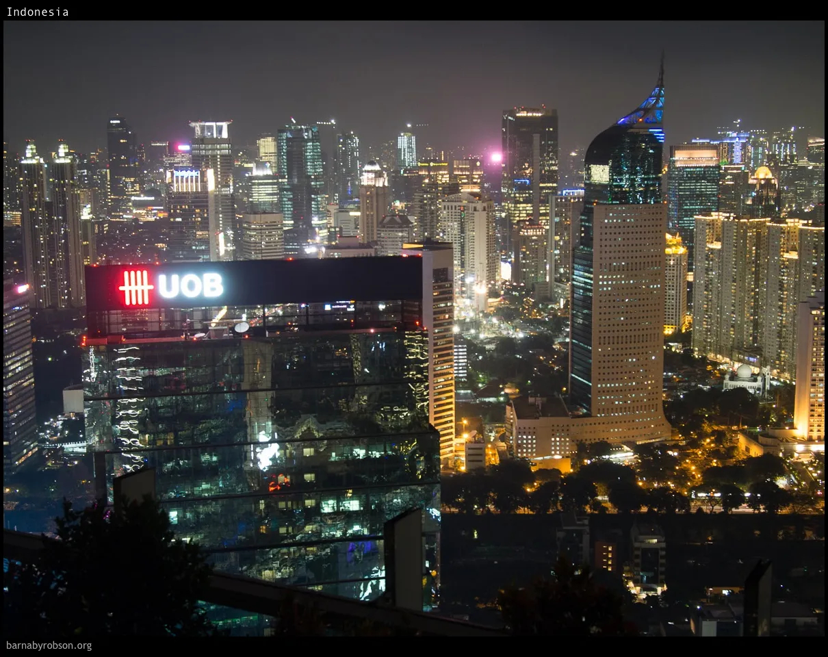 Nighttime city skyline with illuminated UOB building and a tall, pointed skyscraper.