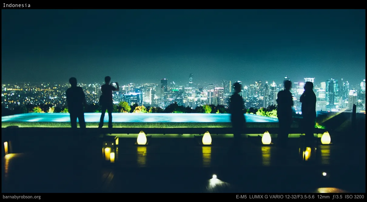 Five silhouetted people on a deck, infinity pool, and city lights at night.