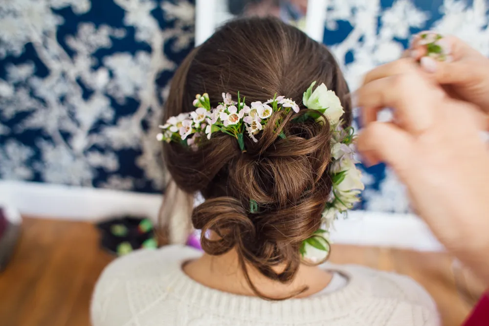 Brown hair updo with flowers being styled by hands.