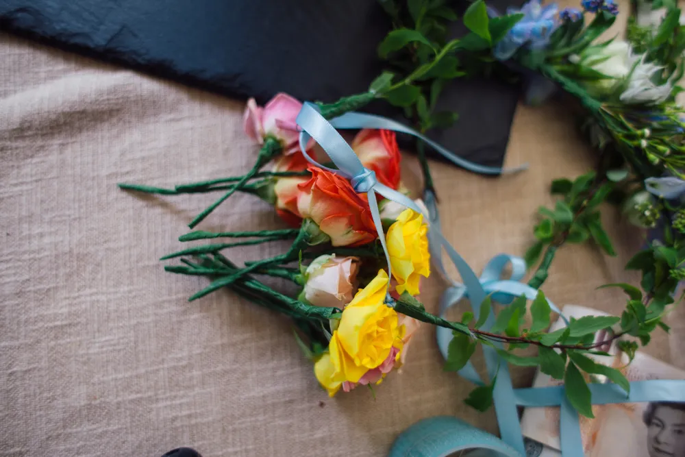Colourful rose buttonholes and a floral wreath with blue ribbons.