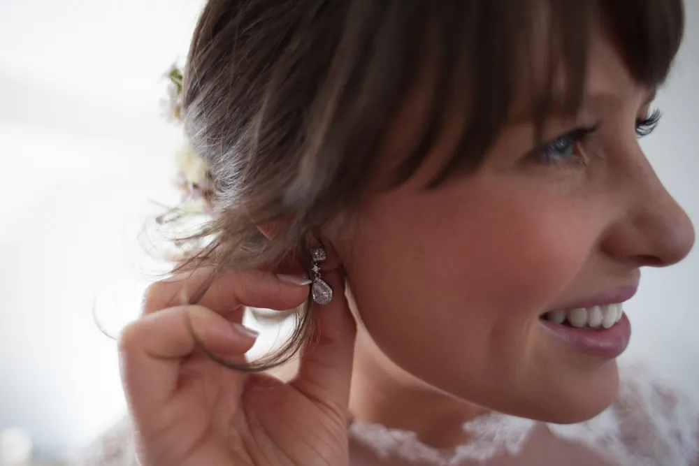 Smiling woman adjusting a sparkling drop earring at her ear.