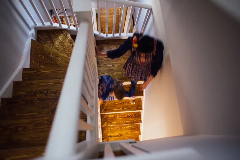 Blurred adult and child descending a wooden staircase with white banisters.