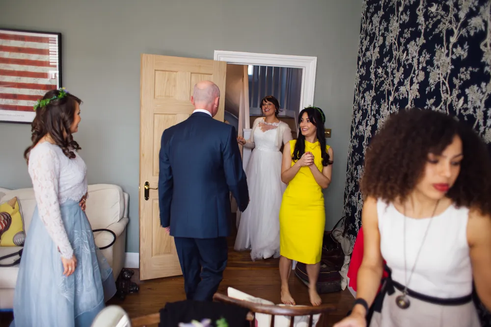 Man in suit approaches doorway, bride and women smiling.