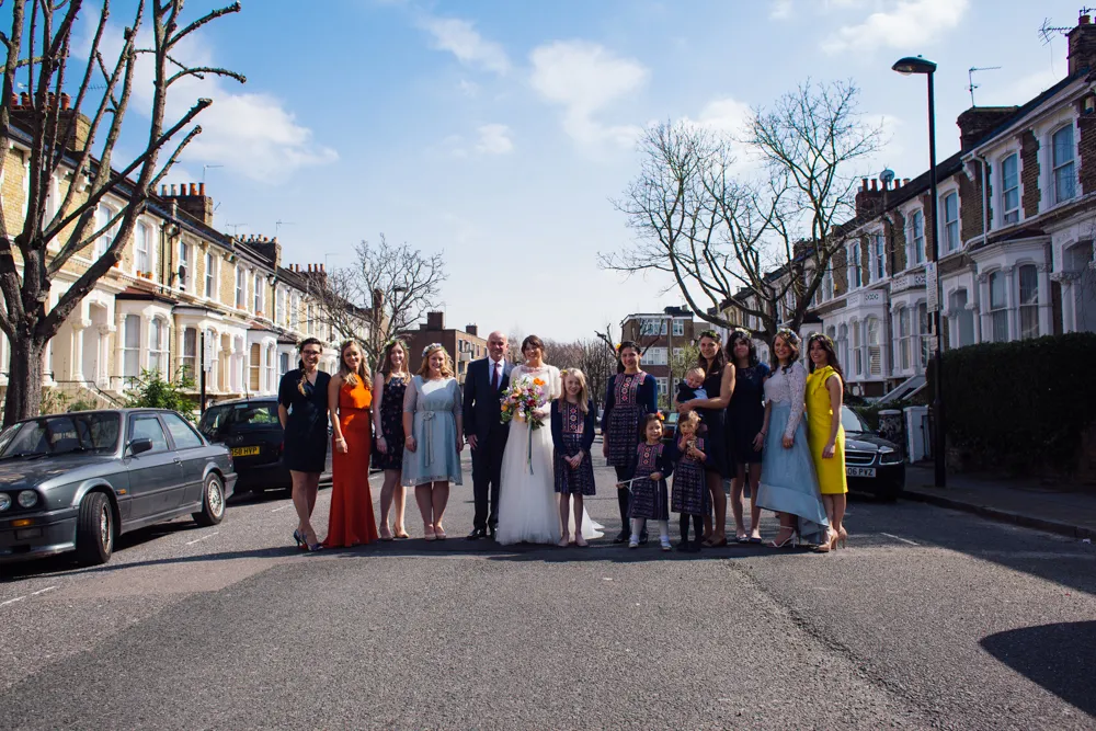 Wedding group in a British street, flanked by terraced houses and bare trees.