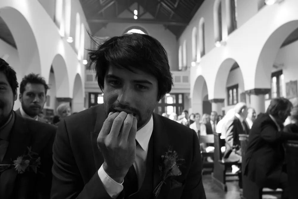 Black and white: Anxious man in suit biting nails, guests in church.