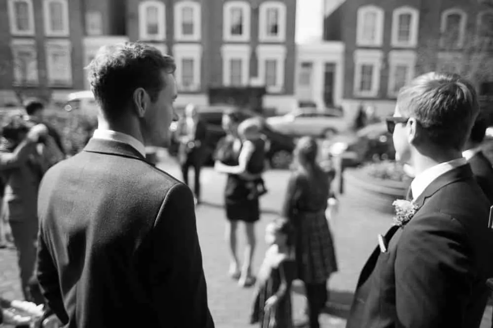 Two men in suits, one with sunglasses, observing a street.