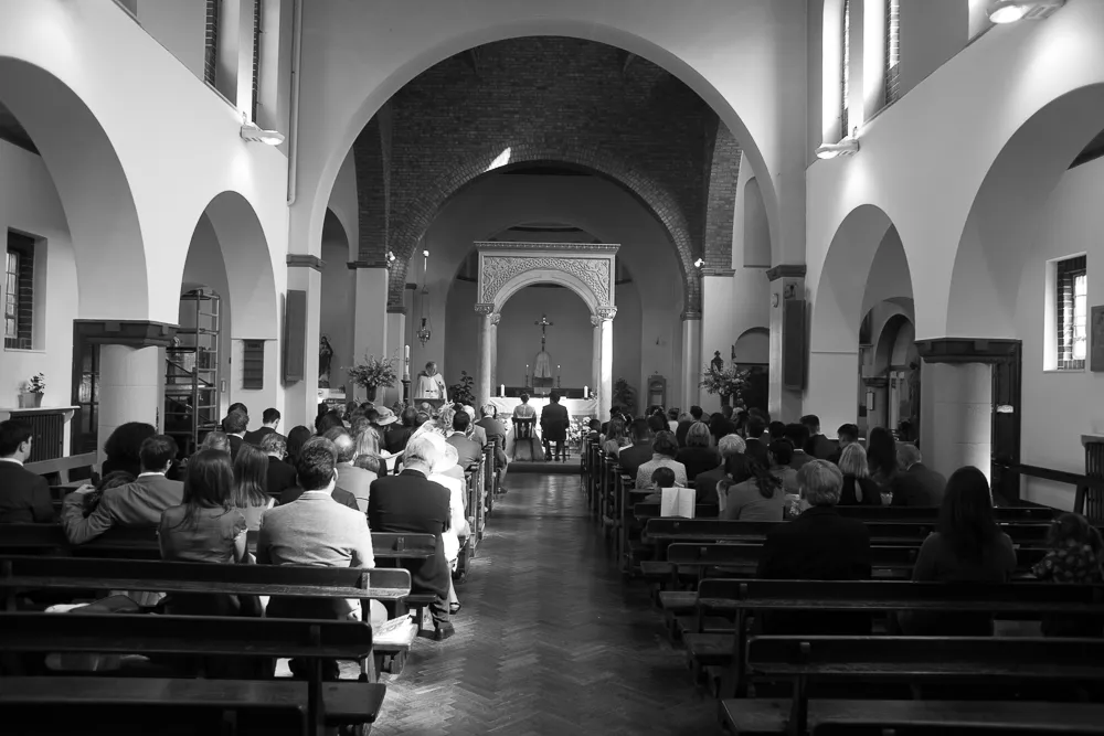 Congregation seated in pews inside a church, priest and couple at altar.