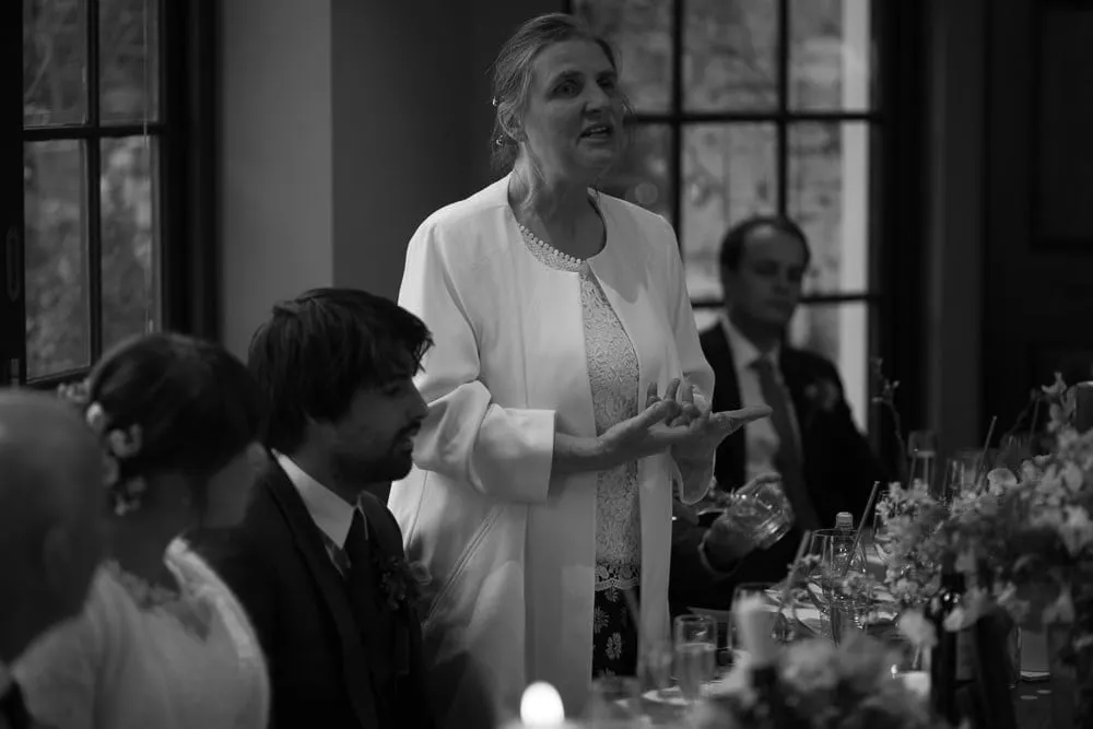 Black and white: woman in white speaks, gesturing, at a formal event.