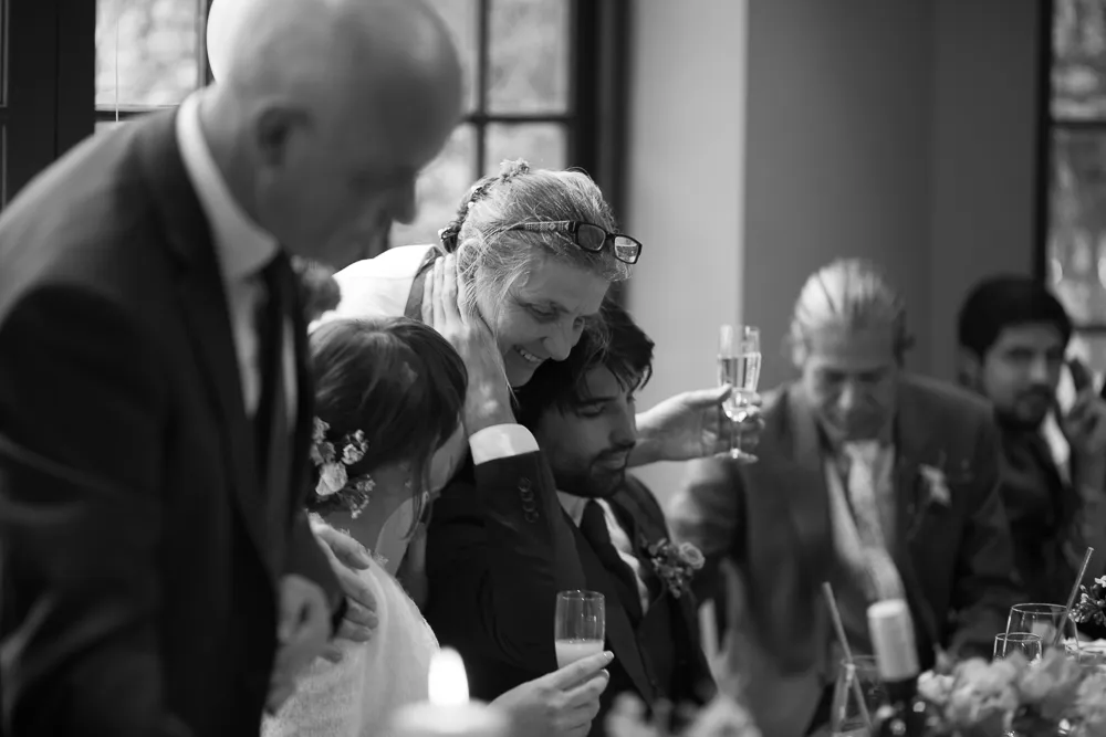Black and white: Smiling woman embraces man, champagne glasses at a reception.