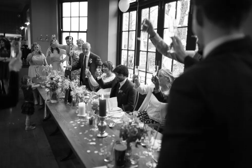 Black and white: Guests raising glasses for a toast at a long table.
