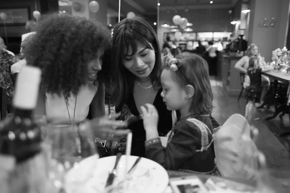 Two women and a child smiling at a table, black and white.