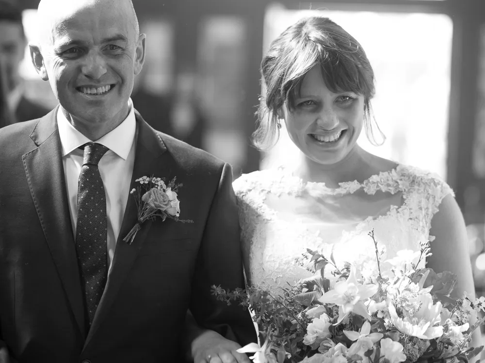 Smiling man in suit and bride in lace dress holding a wedding bouquet.