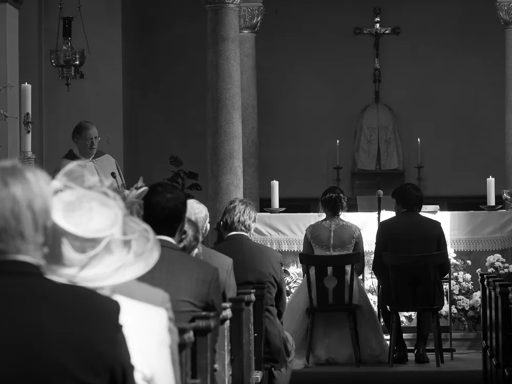 Black and white church wedding: priest, seated couple, and guests.