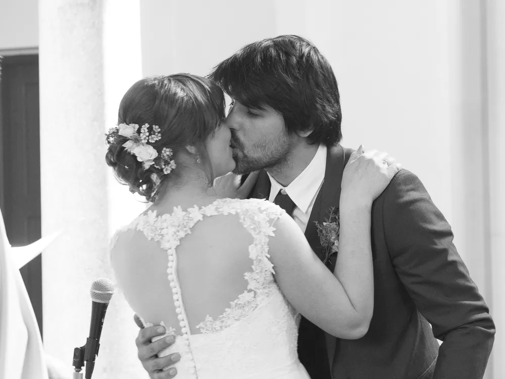 Wedding couple kissing, bride in lace dress with floral hairpiece, groom in suit.