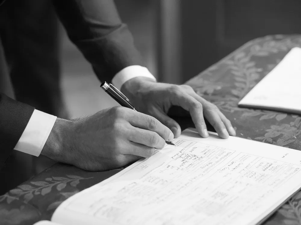 Person in suit signing a document with a pen.