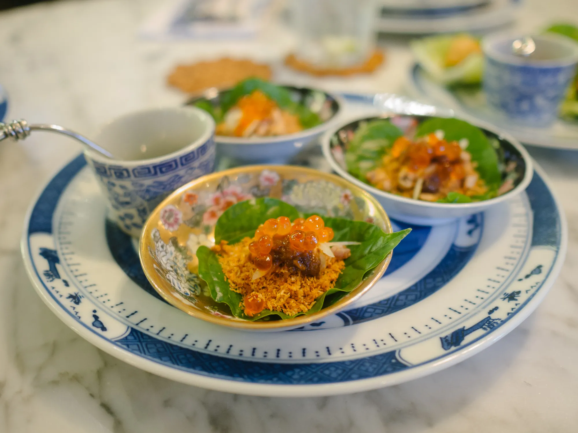 Three small bowls of food with orange roe on a blue and white plate.