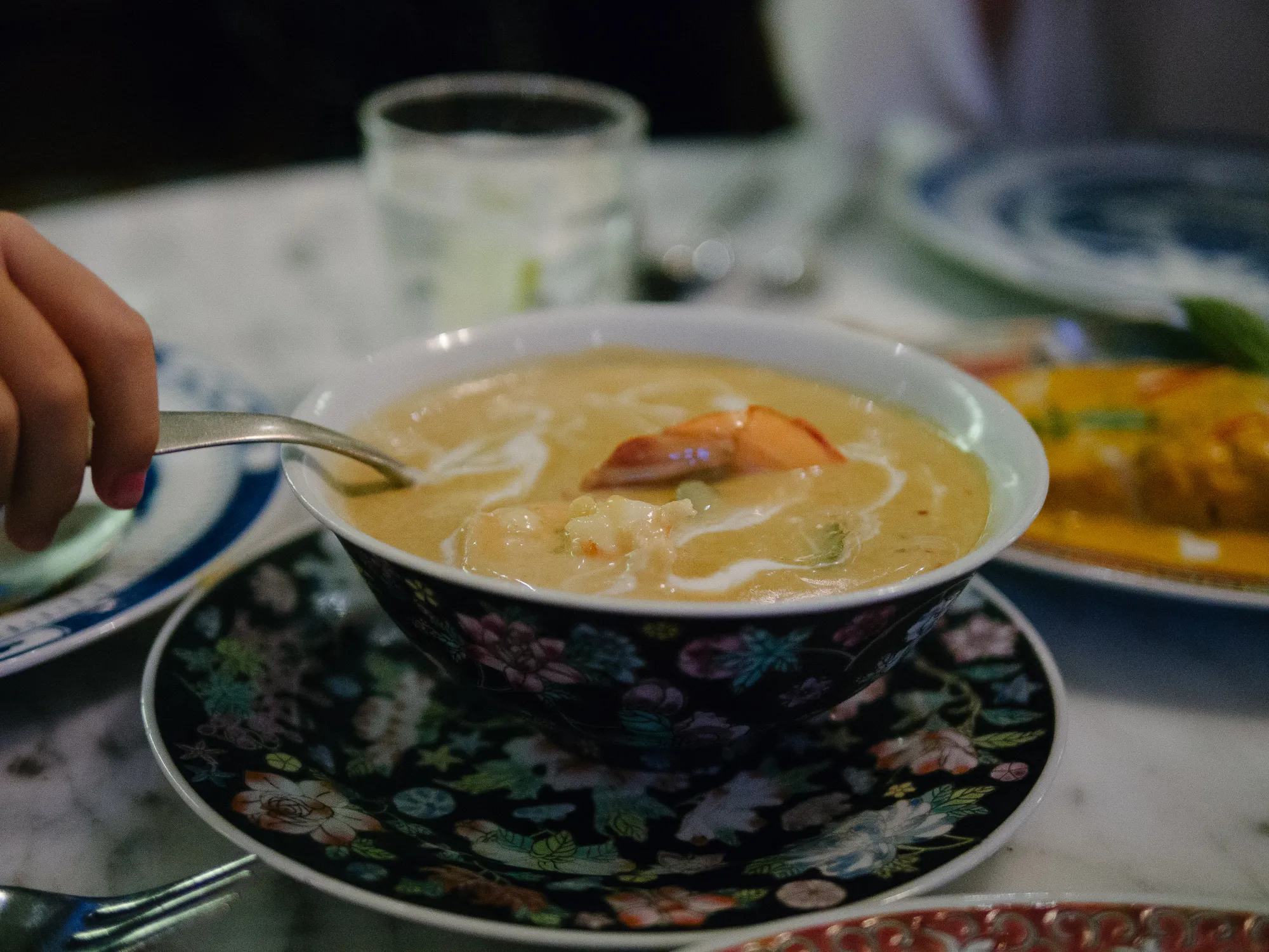 Hand with spoon scooping creamy prawn soup from a floral bowl.