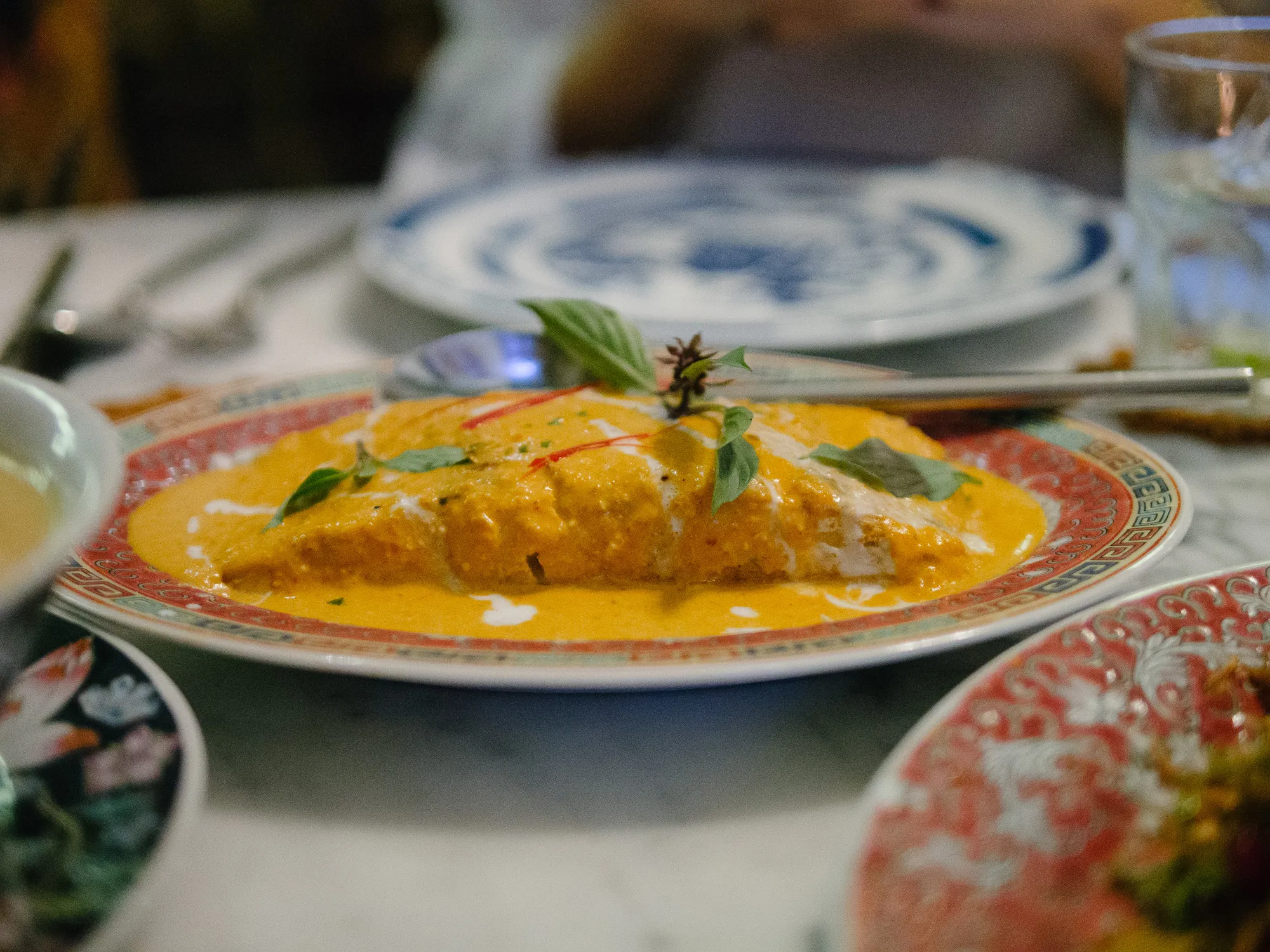 Orange curry dish garnished with basil and chilli on a patterned plate.