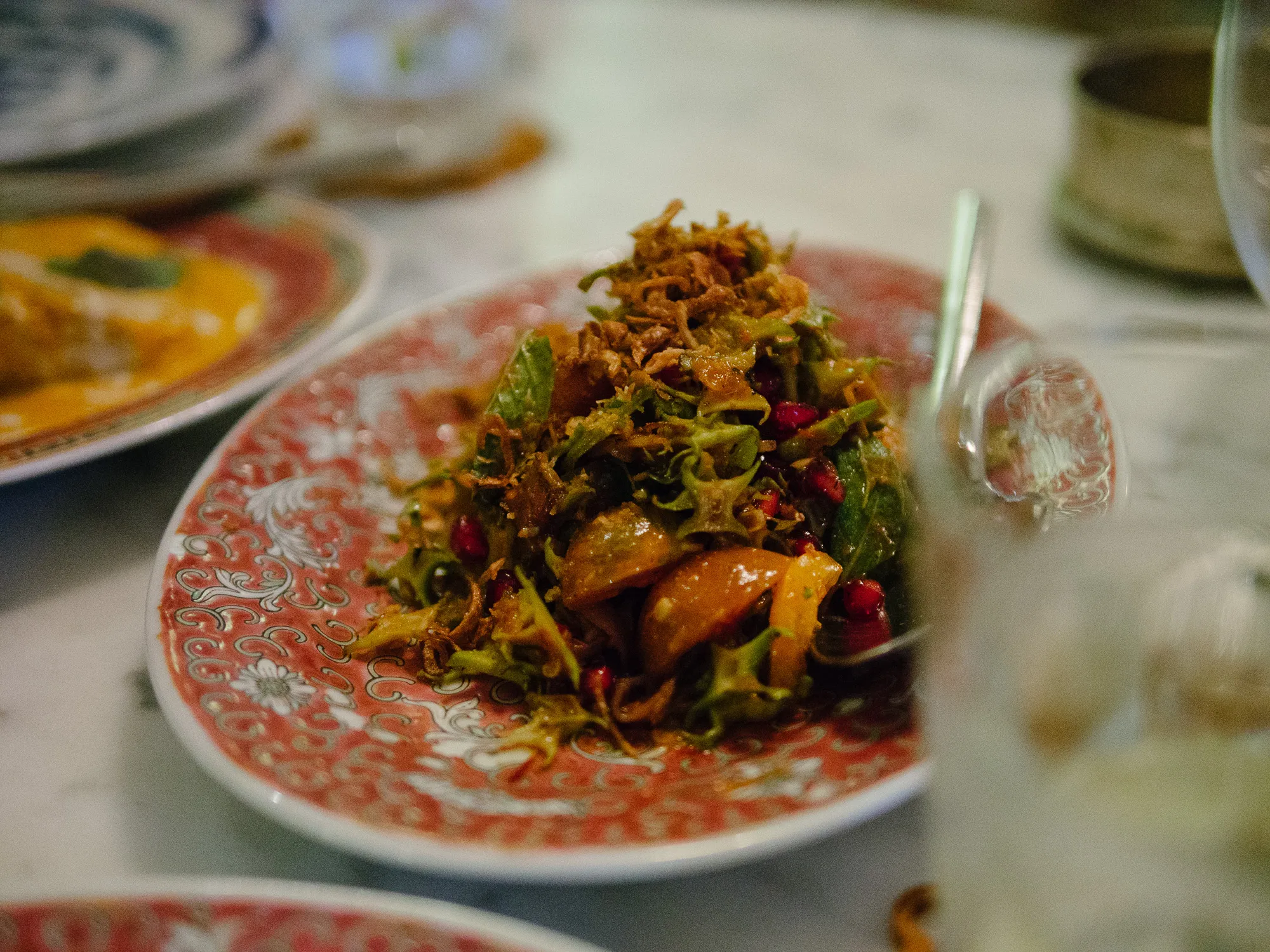 Winged bean salad with pomegranate, orange pieces, and crispy topping on a red plate.