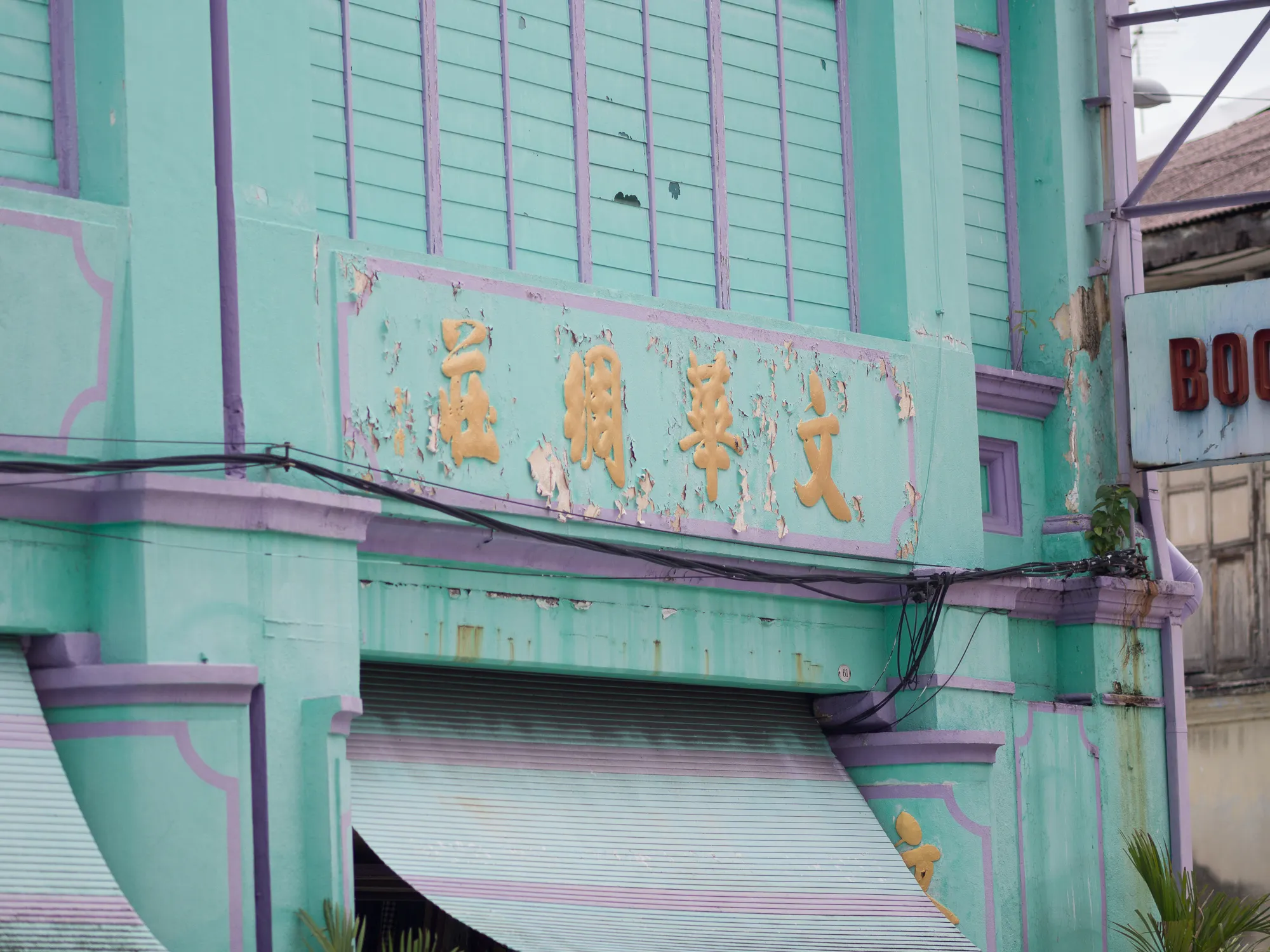 Peeling turquoise and purple building with gold Chinese script and striped awning.