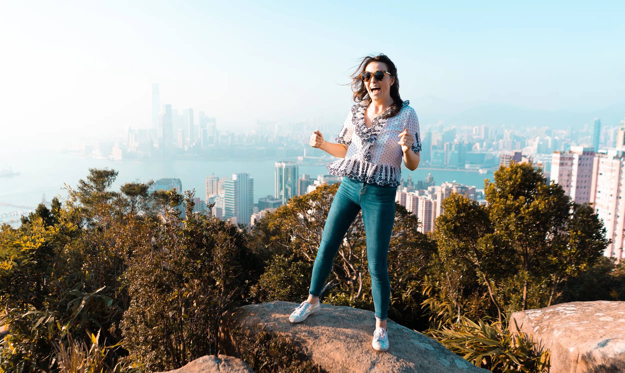 Excited woman on a rock overlooking a city skyline and harbour.