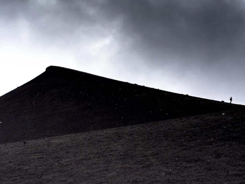 A lone figure on the black cinder slope of Etna under heavy cloud
