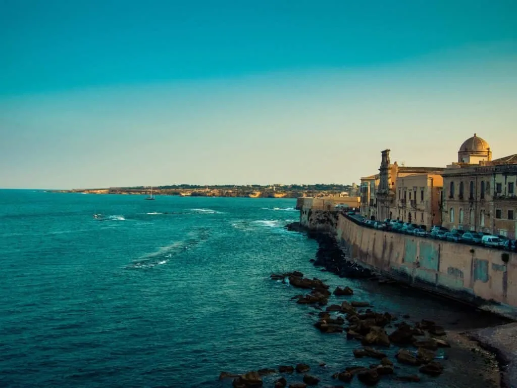 The Ortygia seafront, teal water breaking below the old wall
