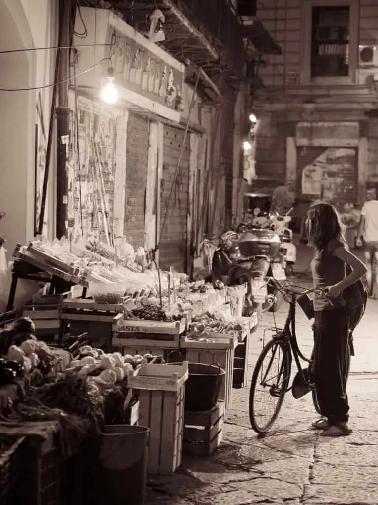 A cyclist pauses at a fruit stall in a Palermo street market