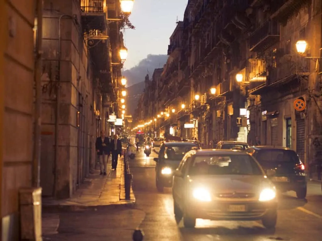 Evening traffic threading down a lamp-lit Palermo street