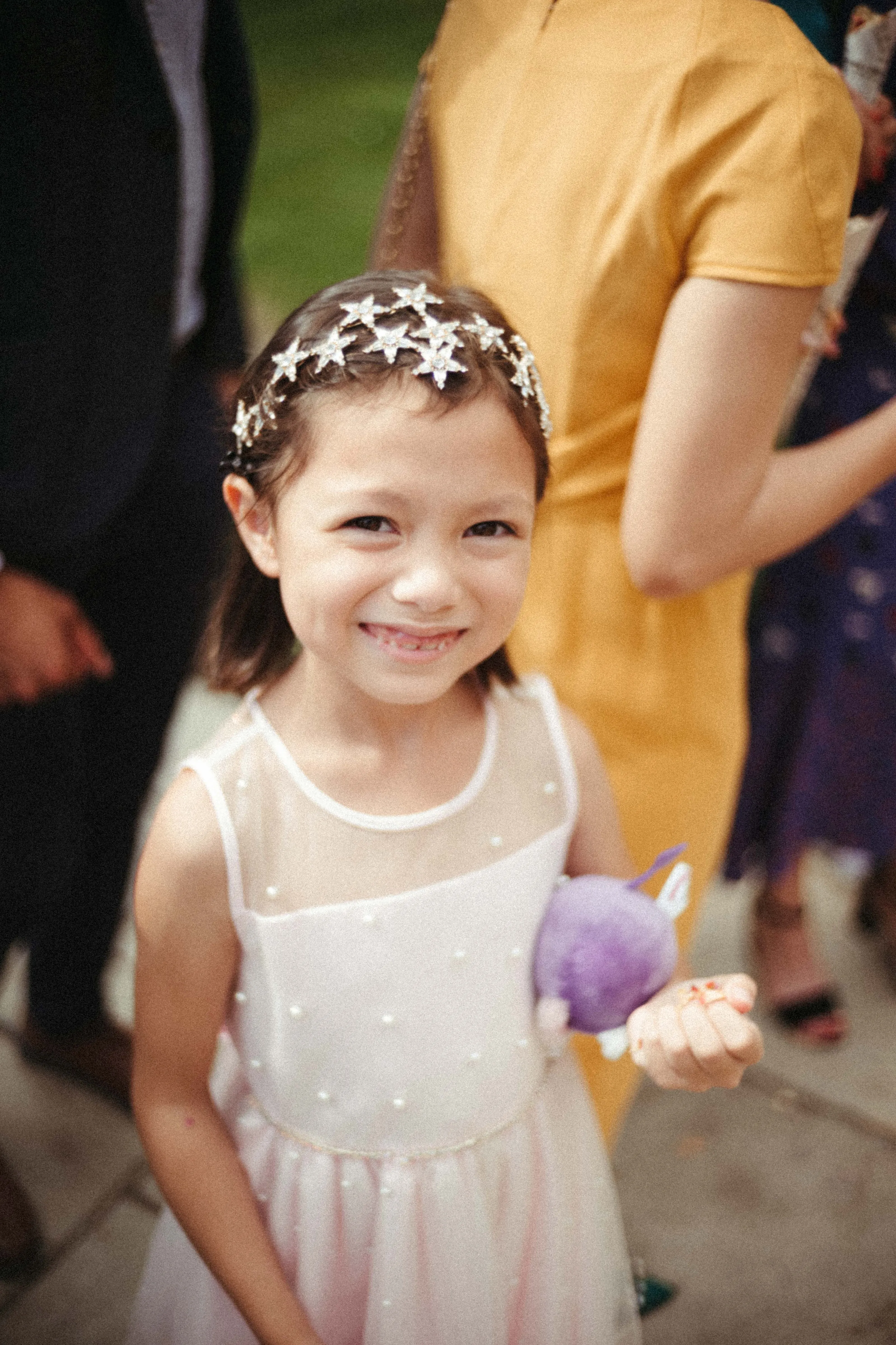 Smiling girl with star headband, pink dress, holding a purple plush toy.