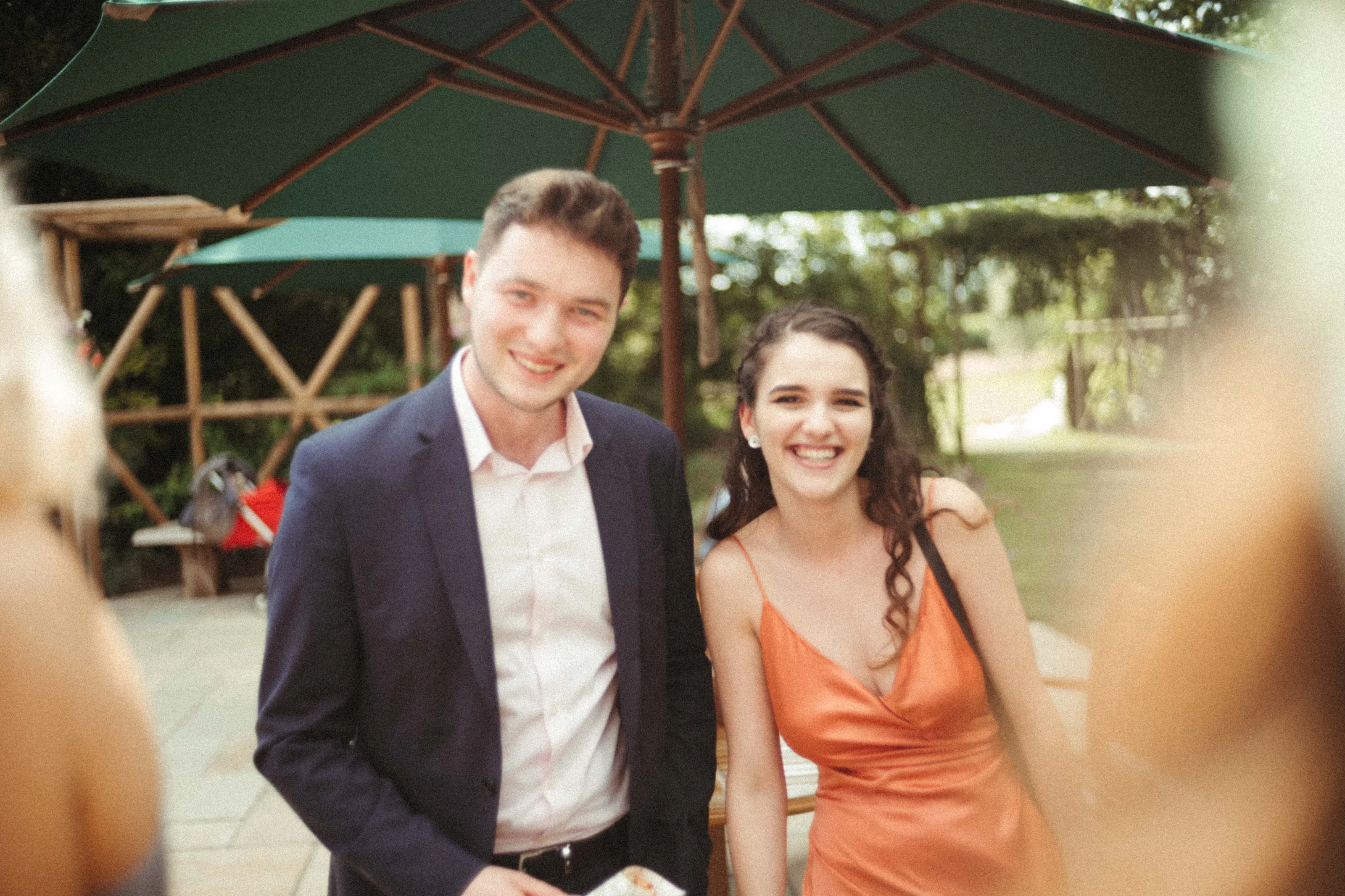 Smiling man in suit and woman in orange dress under a parasol.