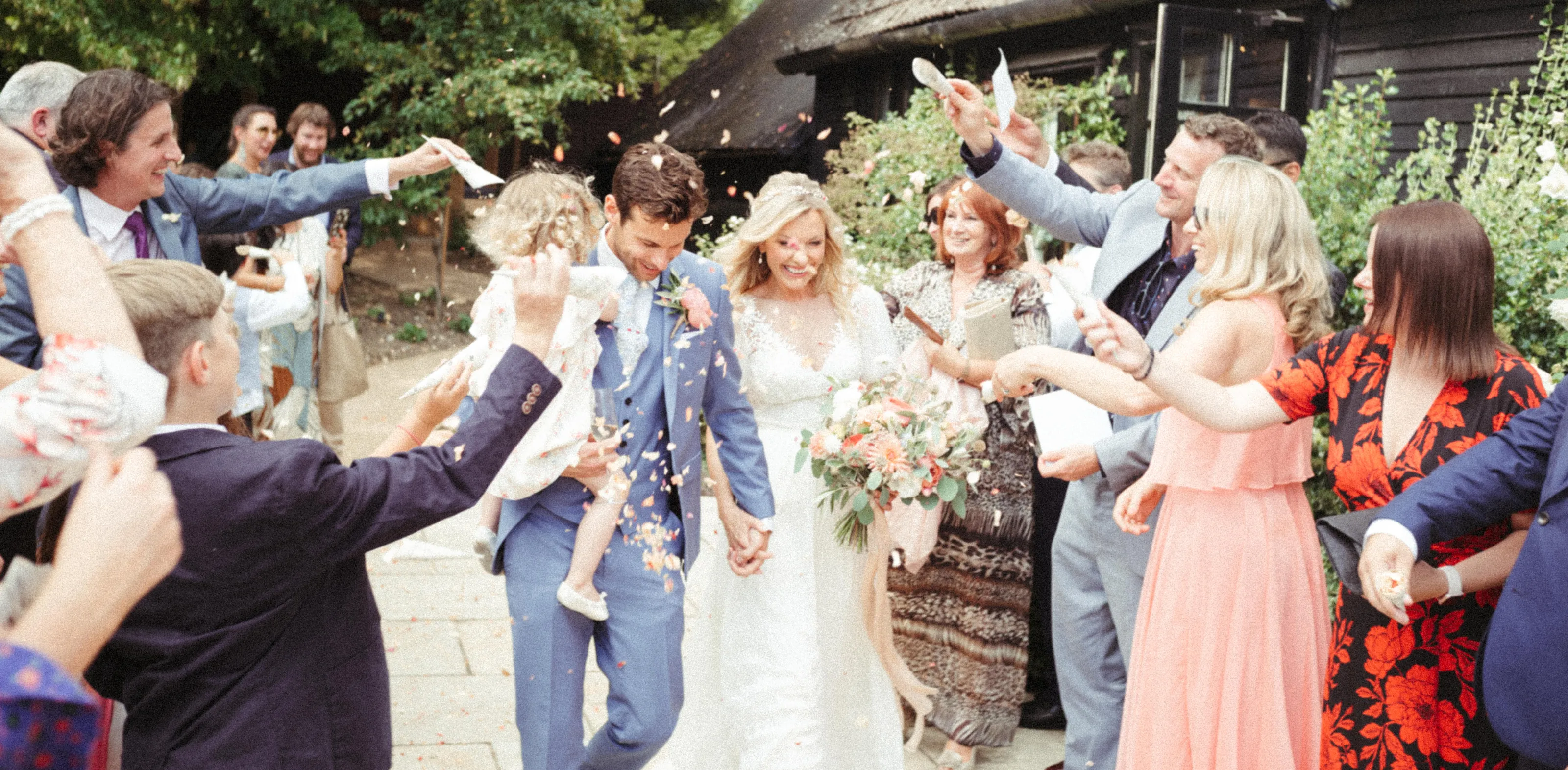 Bride and groom smiling, showered with confetti by guests.