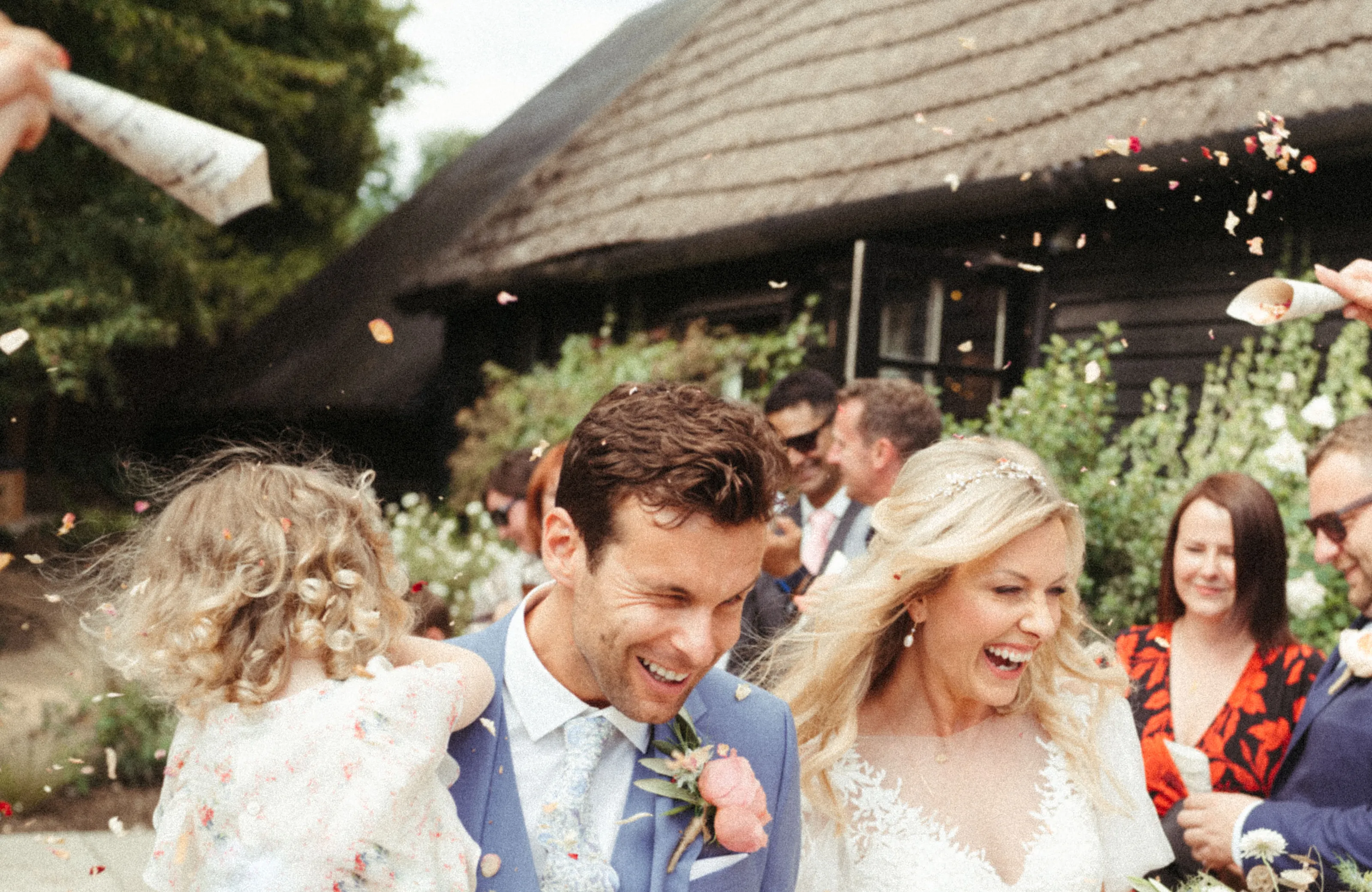 Smiling bride, groom, and child showered with petals at a wedding.