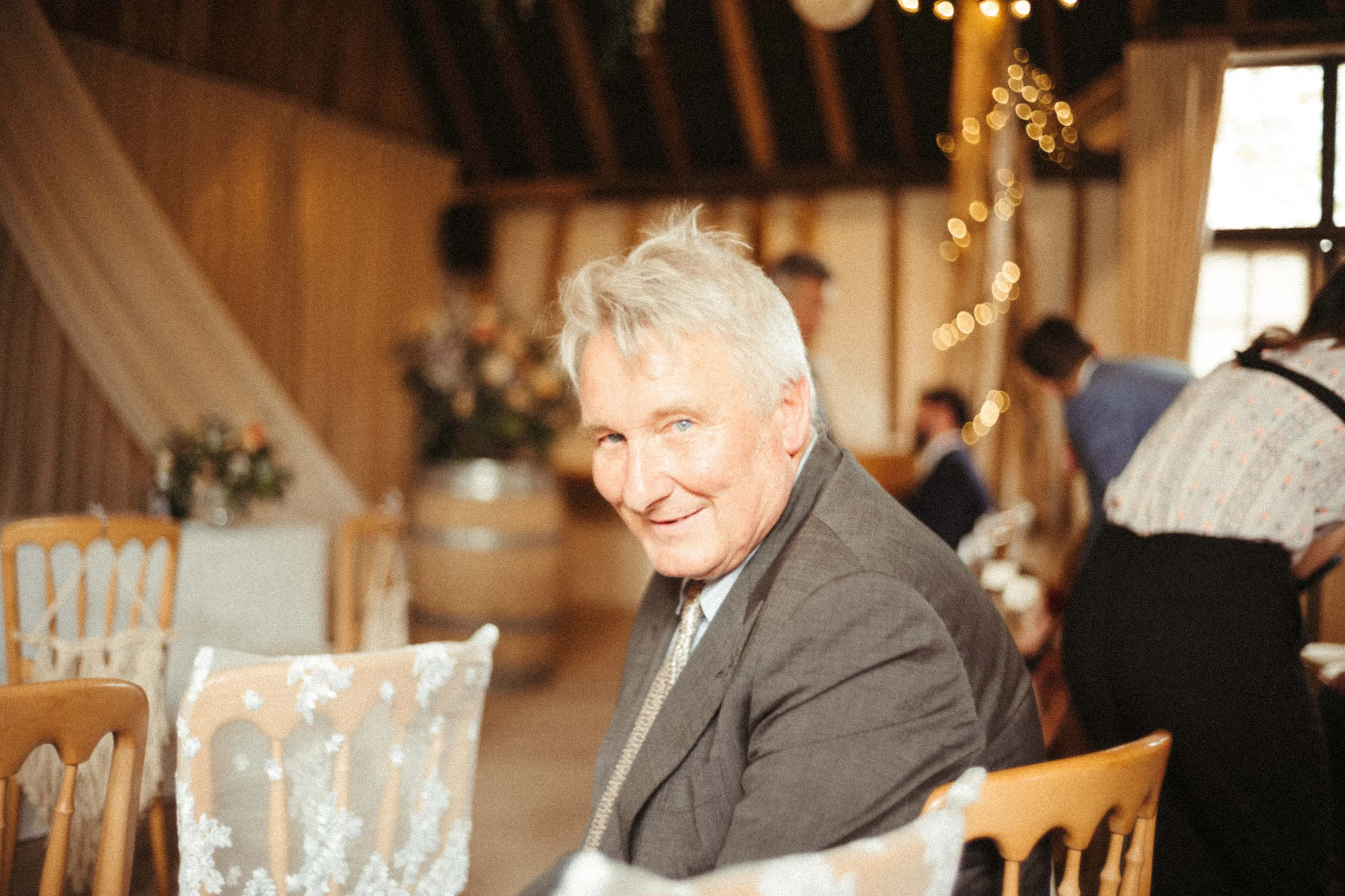 Smiling man with grey hair in a suit at a barn wedding.