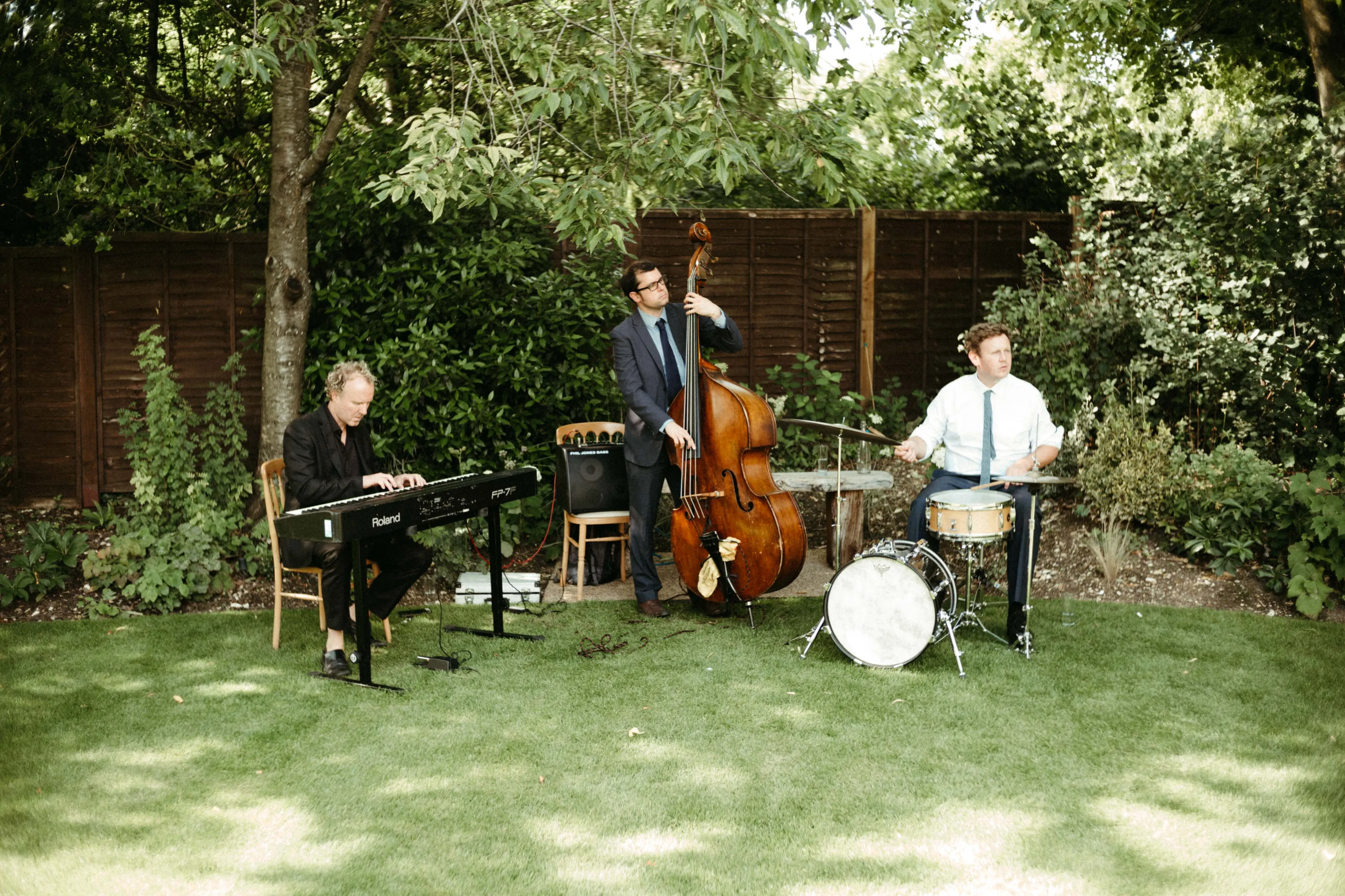 Outdoor band playing keyboard, upright bass, and drums on grass.