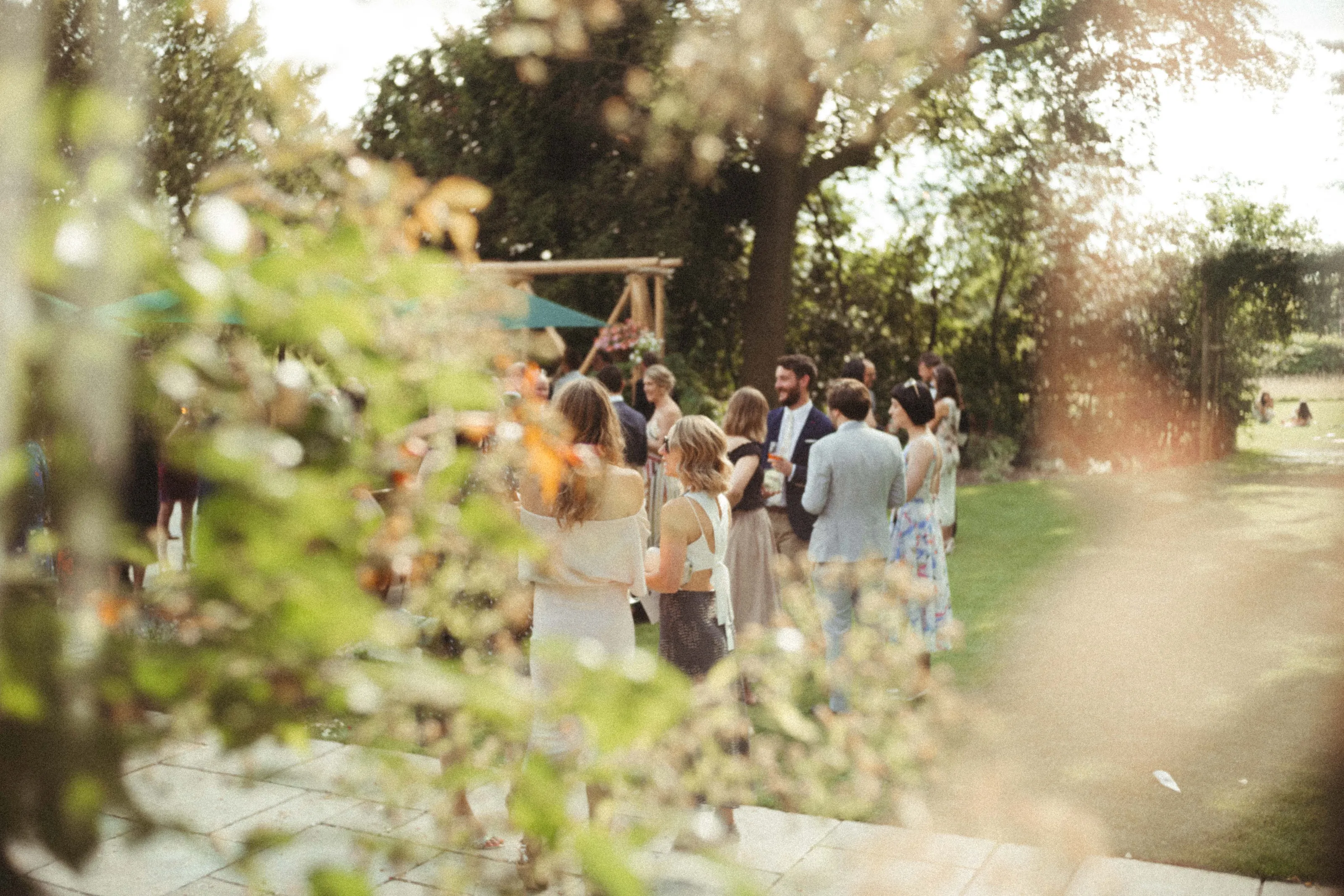 Guests mingling at an outdoor event, framed by blurred green leaves.