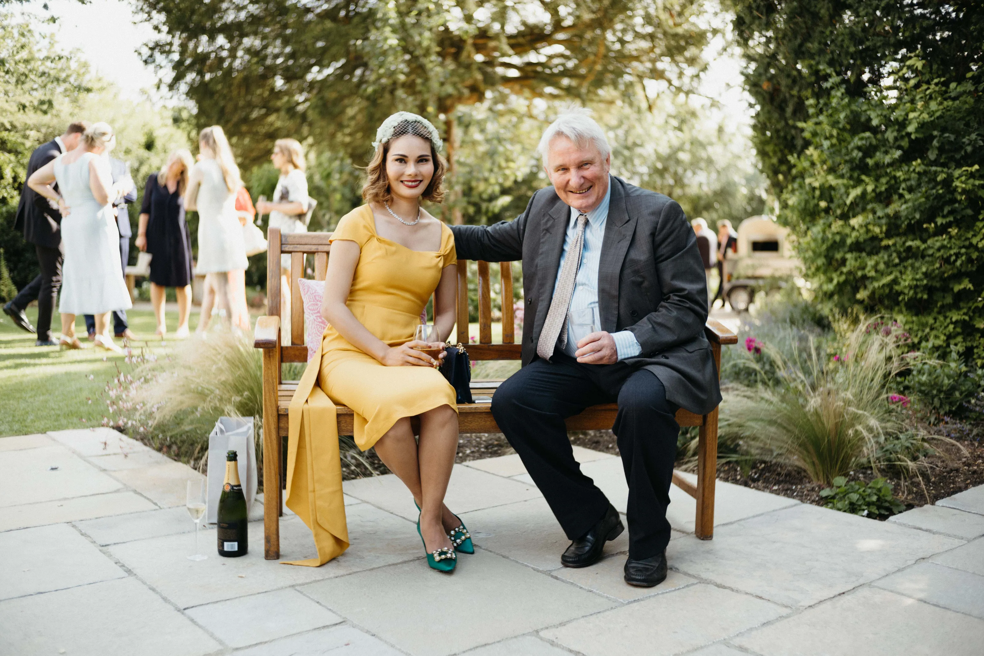 Smiling woman in yellow dress and man in suit on bench outdoors.