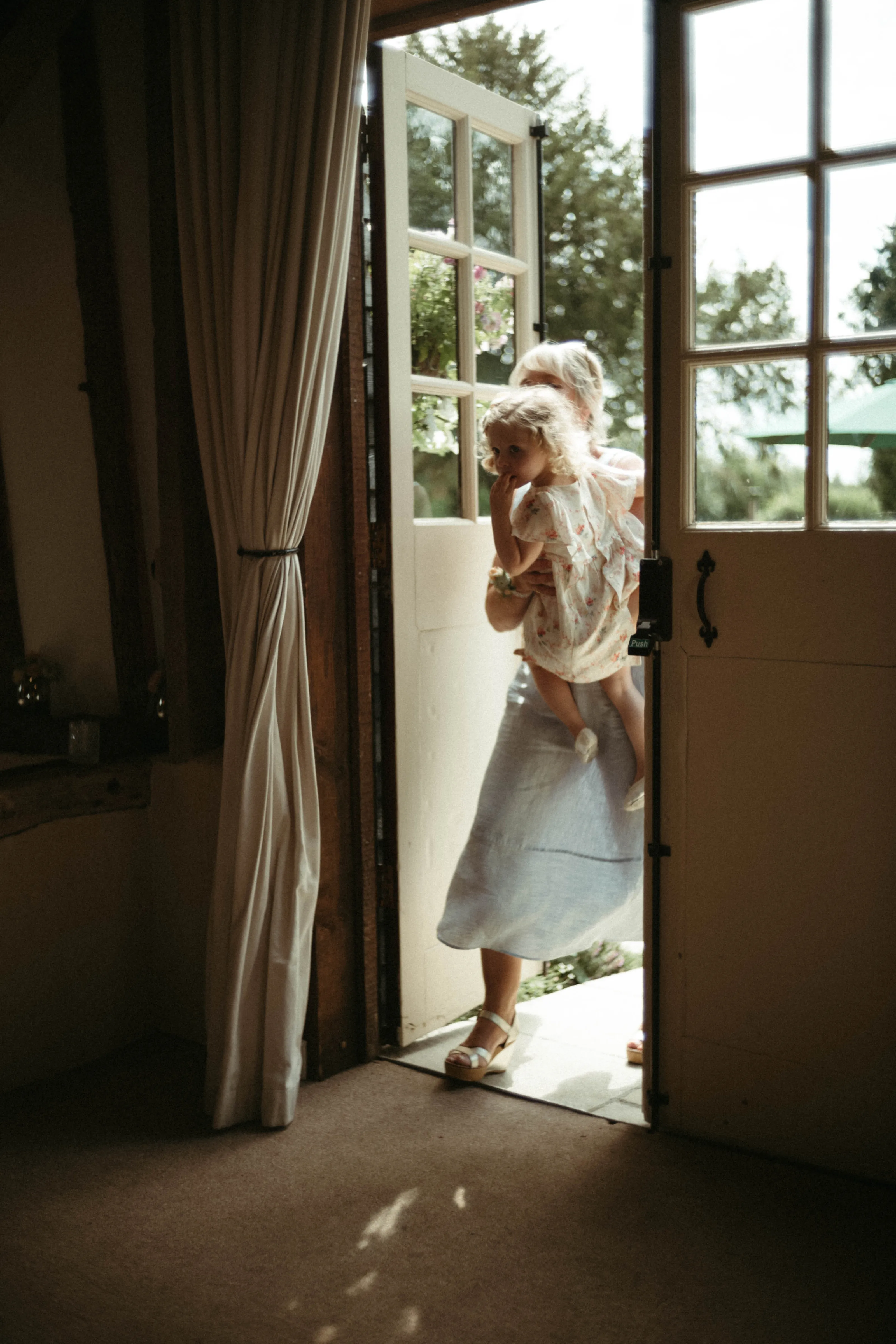 Woman holding a child in a doorway, looking out to a sunny garden.