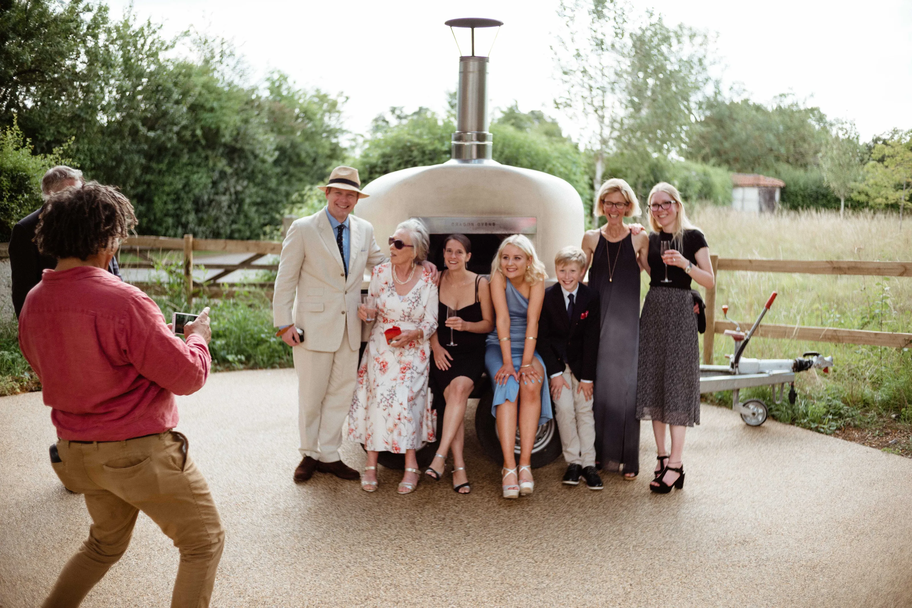 Person photographs group posing with a mobile pizza oven outdoors.