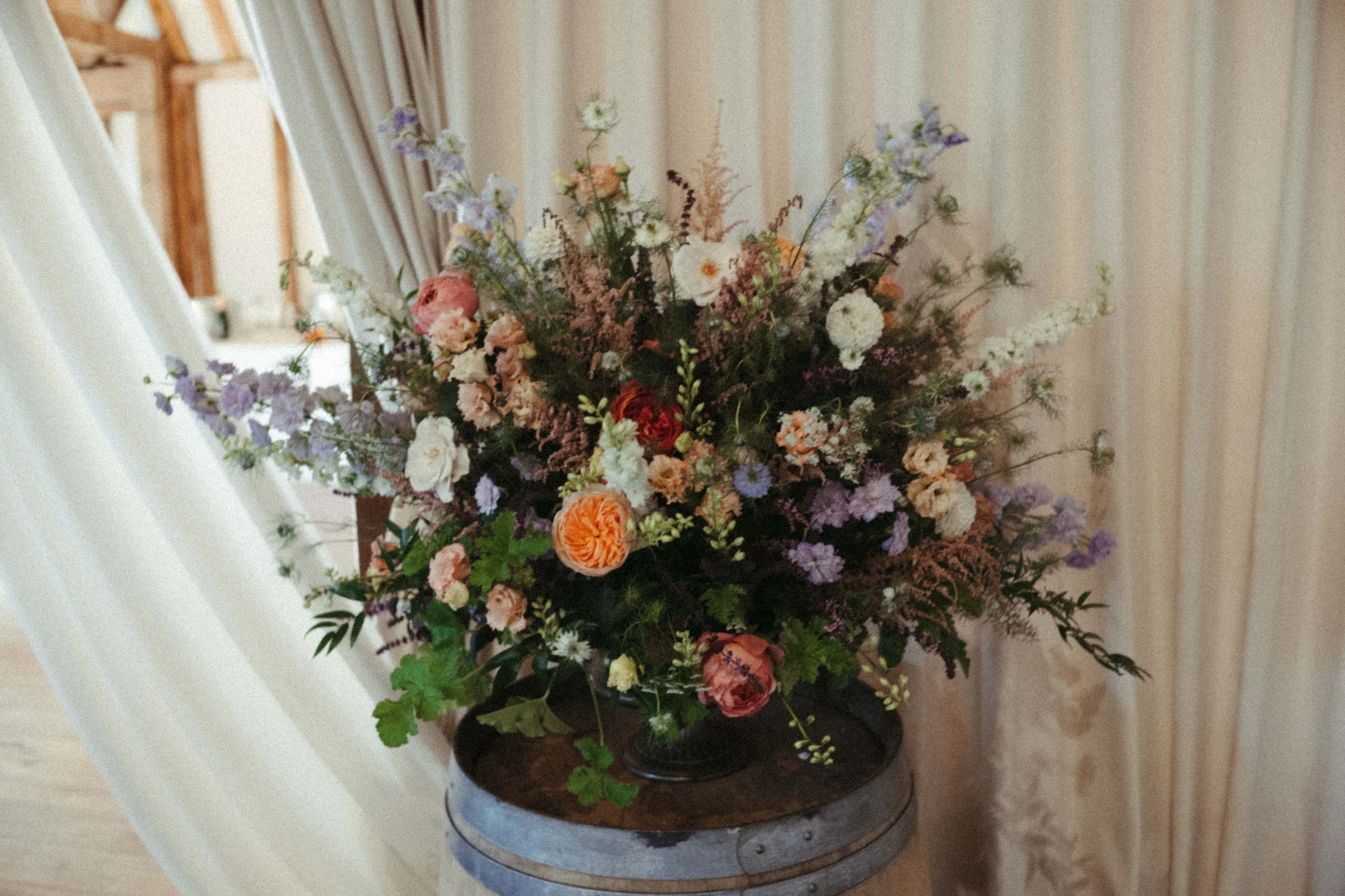 Lush floral display in peach, white, purple on a rustic wooden barrel.