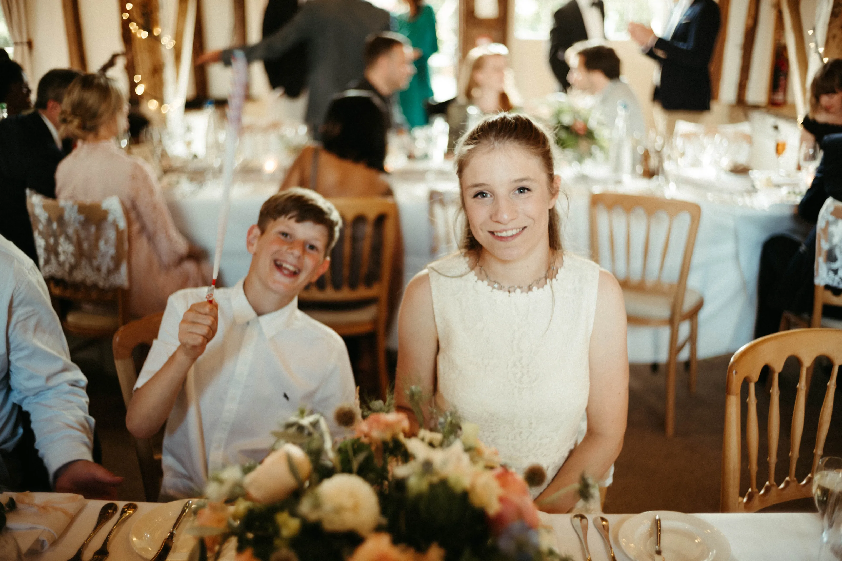Smiling woman and laughing boy at a table with flowers, guests in background.