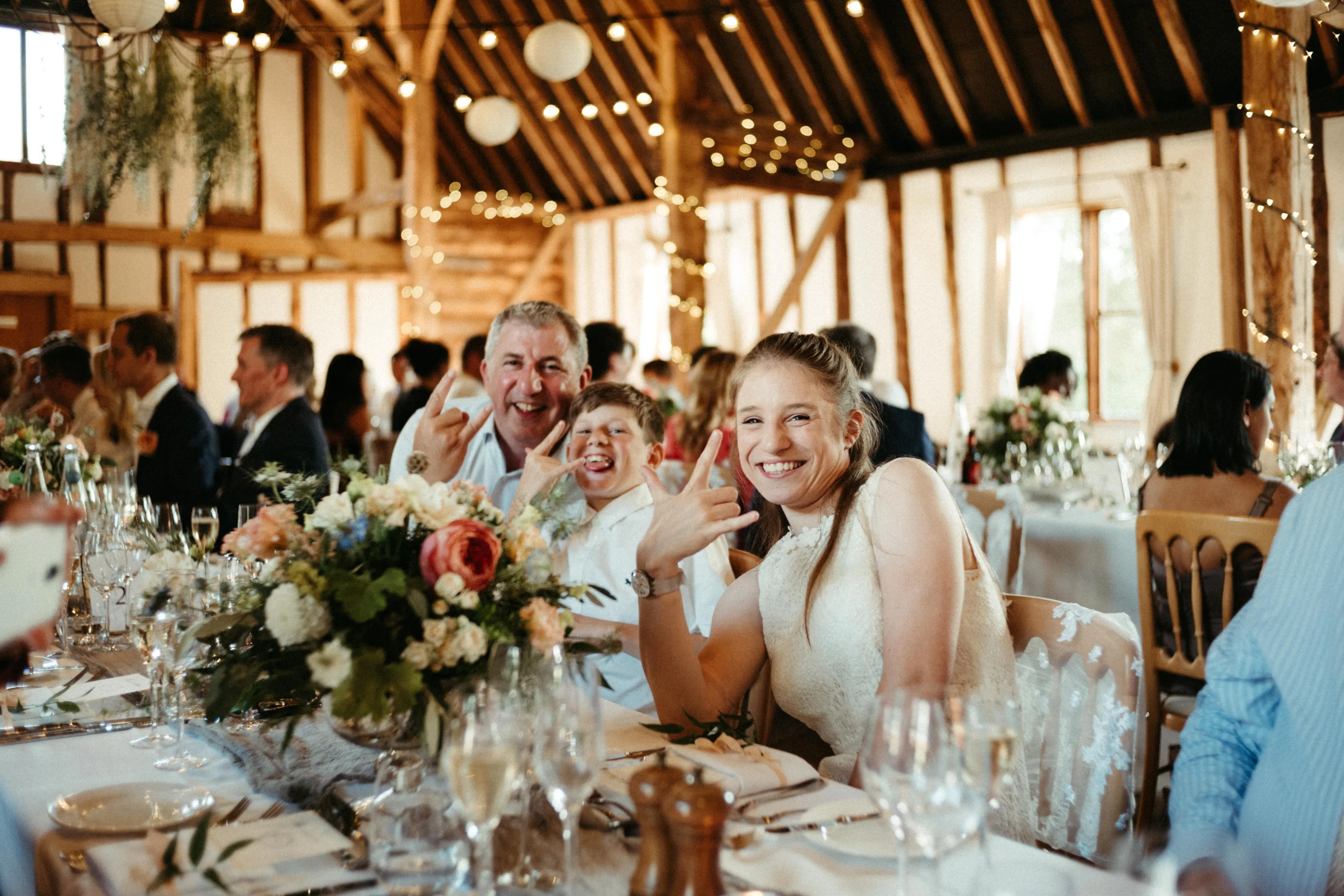 Smiling guests making rock-on gestures at a barn wedding reception.