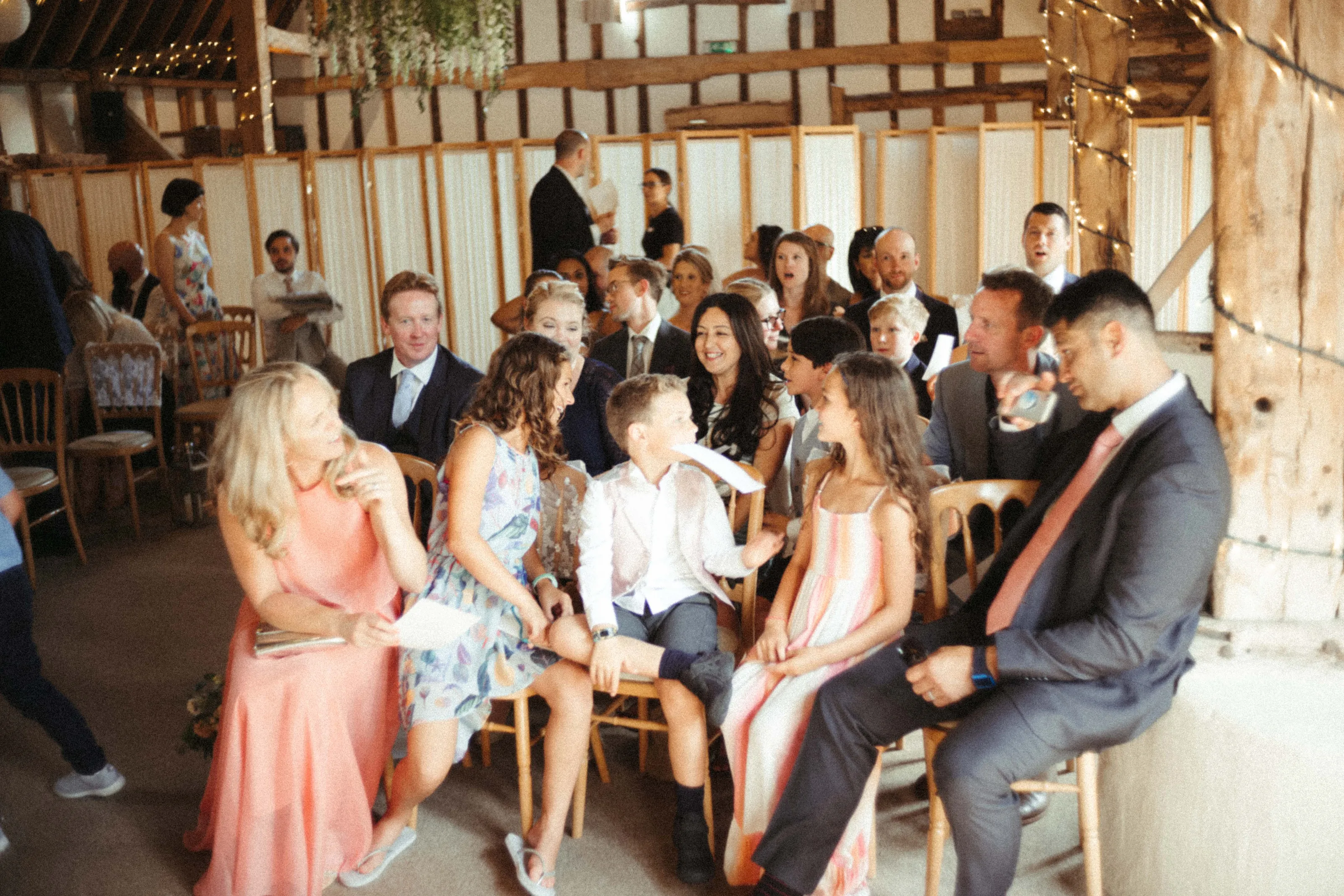 People of all ages seated at a barn event with fairy lights.