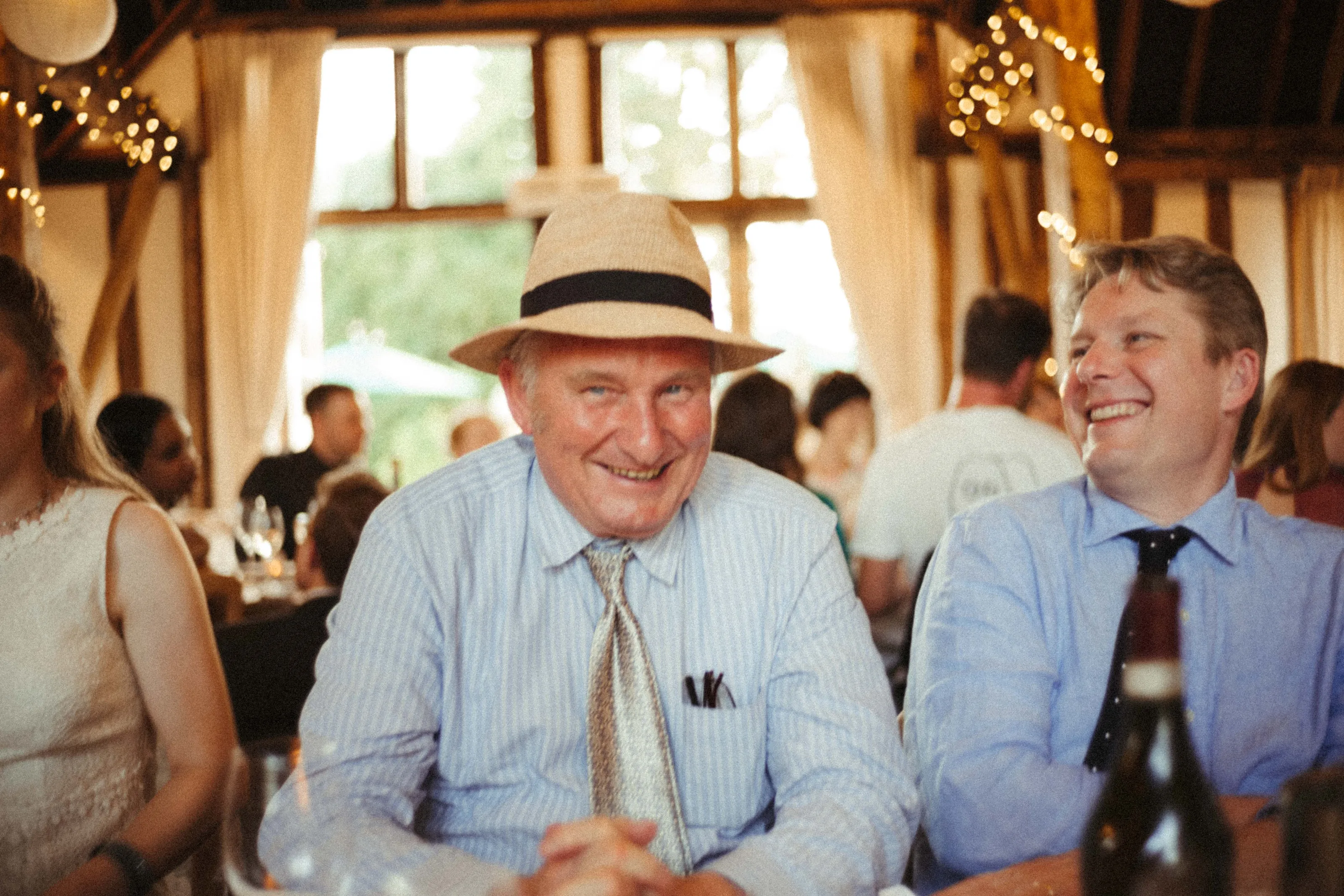 Two smiling men at a table, one wearing a straw hat.