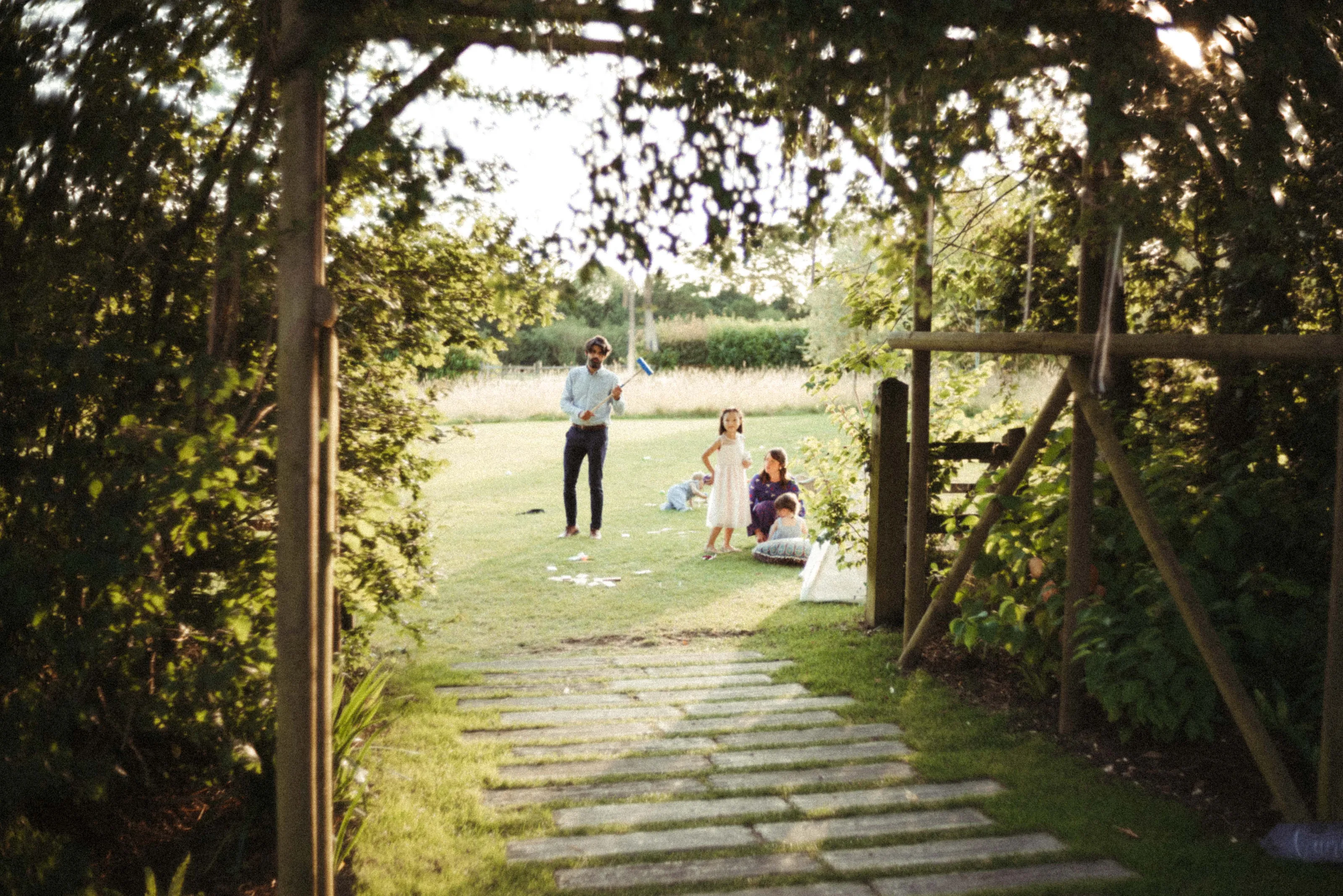 Family playing on a sunny garden lawn with a stepping stone path.