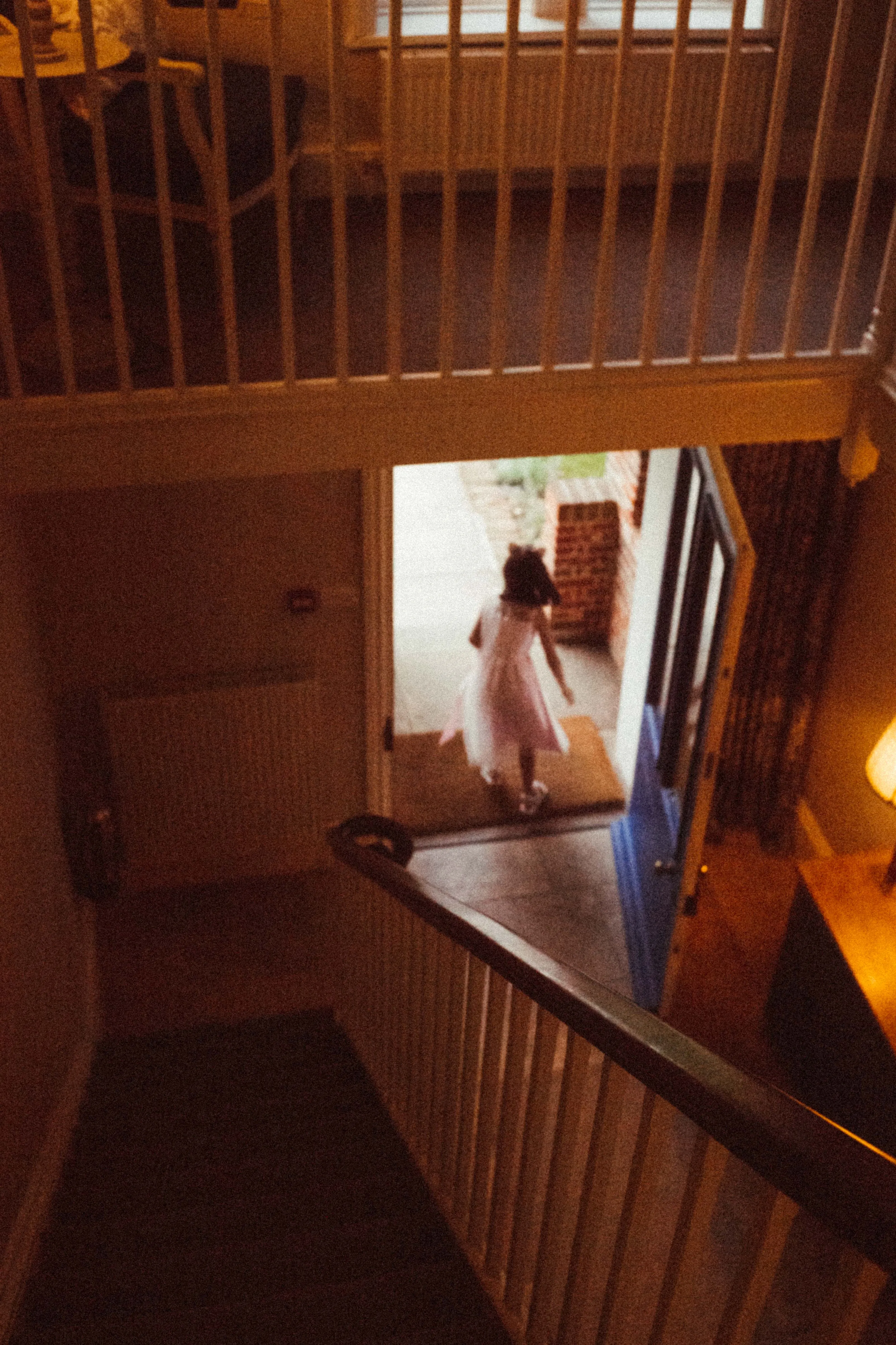 Child in light dress walks through doorway at bottom of stairs.