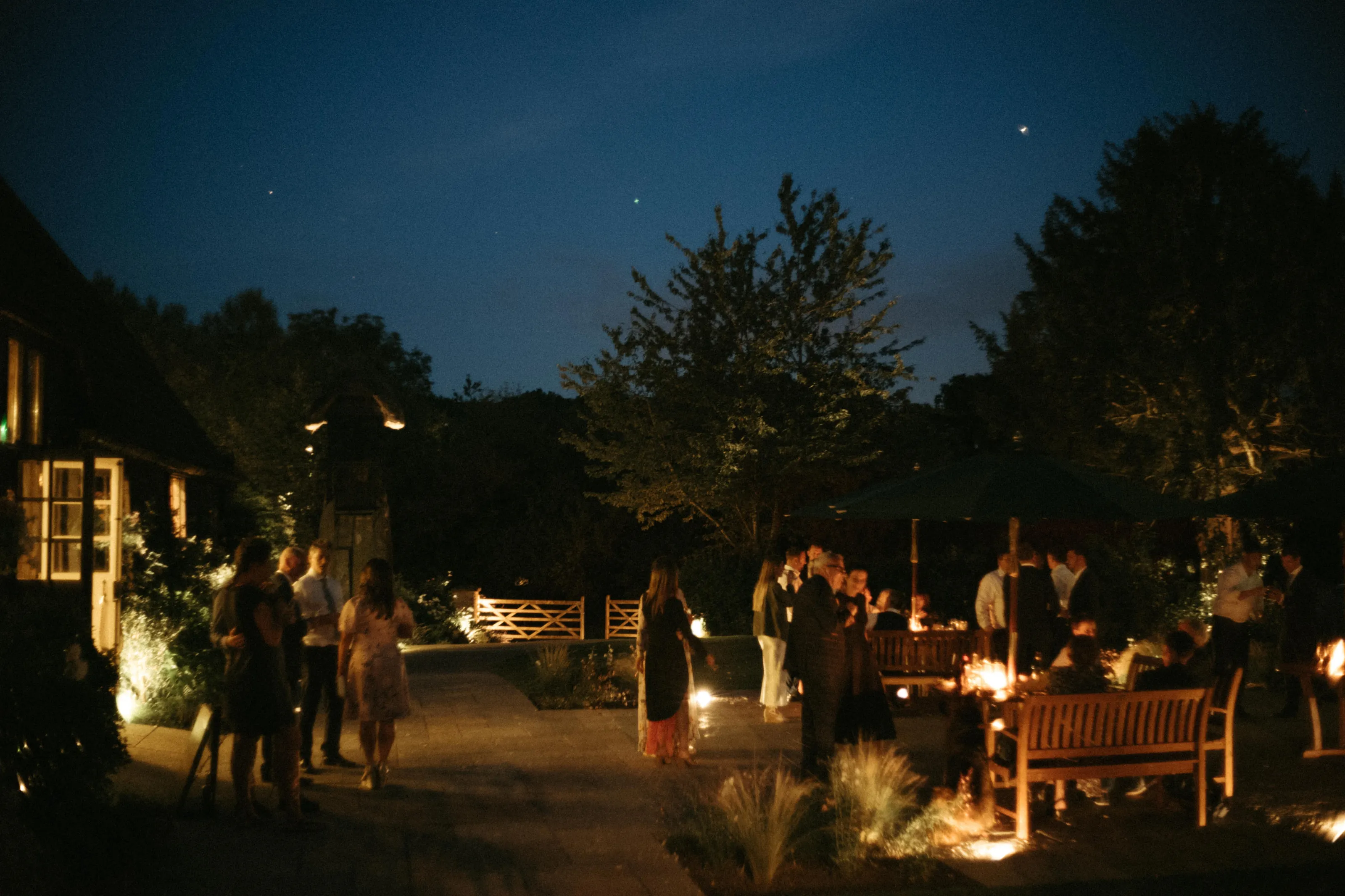 Evening outdoor gathering with people, warm lights, and a starry sky.