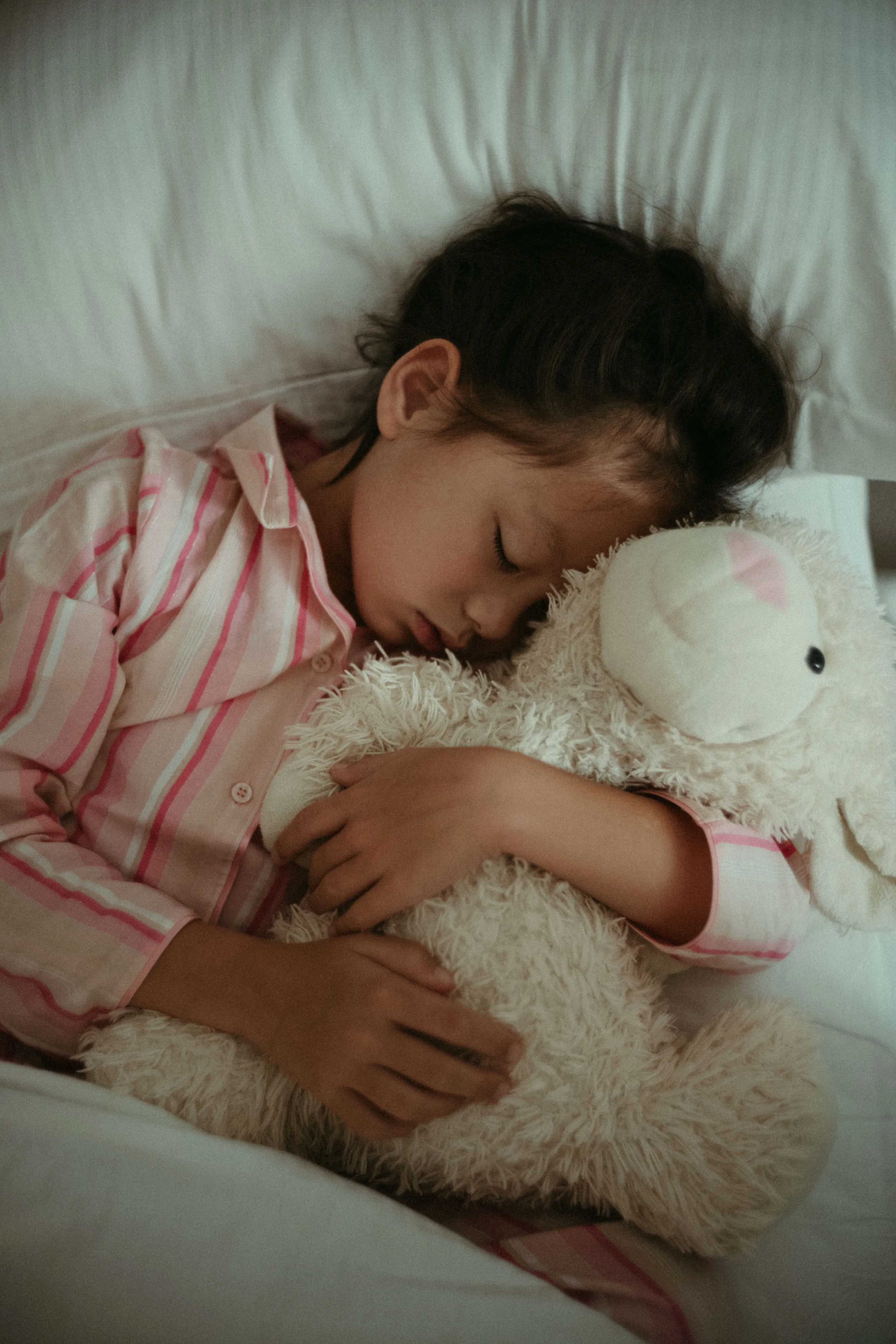 Sleeping child in pink pyjamas, cuddling a white stuffed animal.